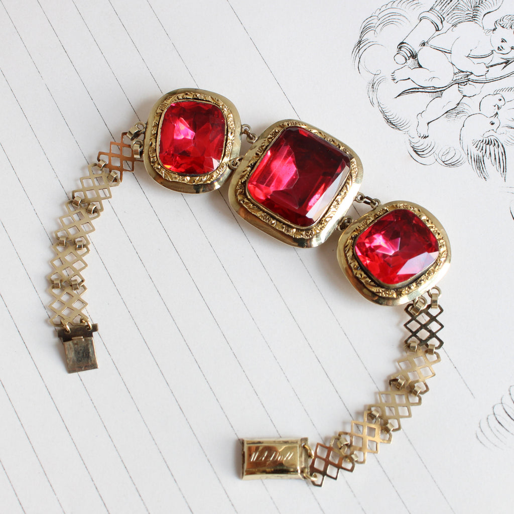 gold bracelet with three large square red stones that are very glittery set in bezels with a lattice filigree wrist strap.