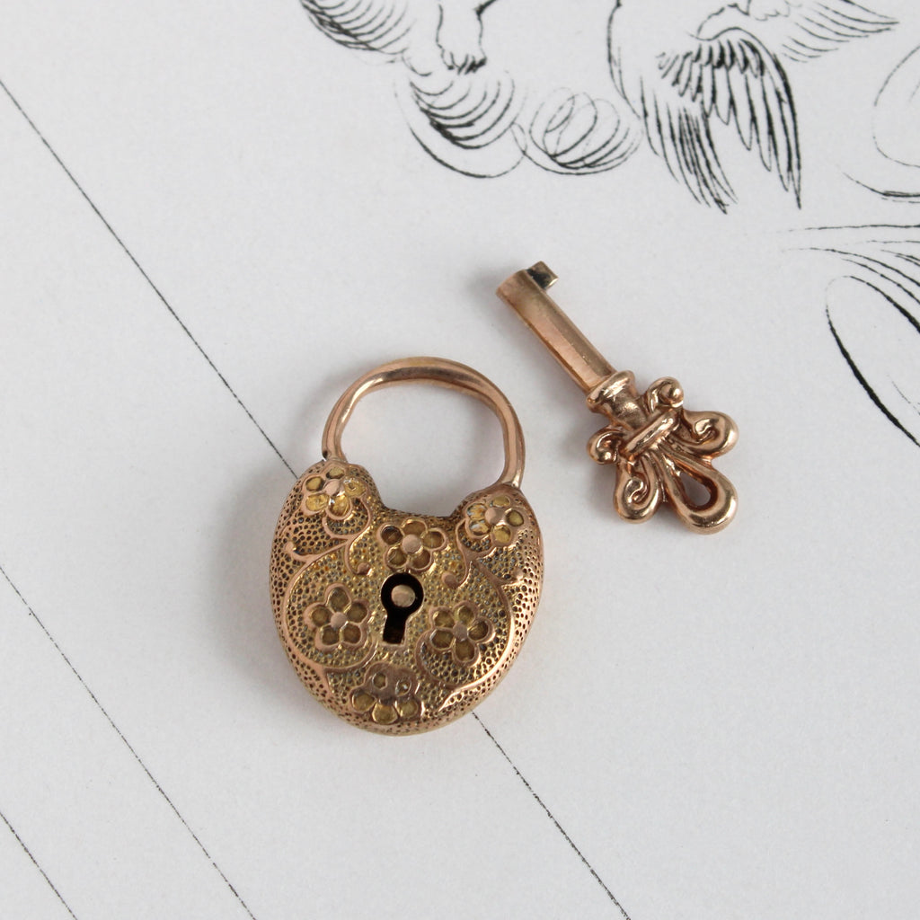 small gold padlock in a heart shape with embossed flowers on the front that opens and locks with a gold key