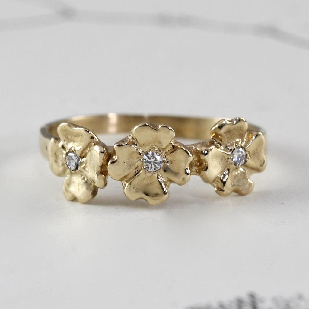 yellow gold ring with three dogwood flowers acroos the front each with diamond centers.
