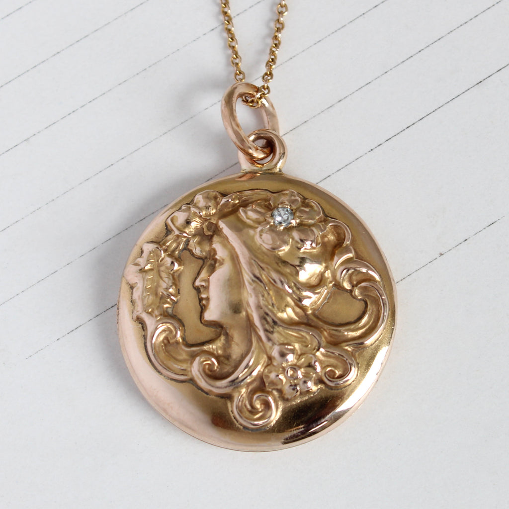 yellow gold locket with the image of a lady with flowers in her curling hair and a diamond accent