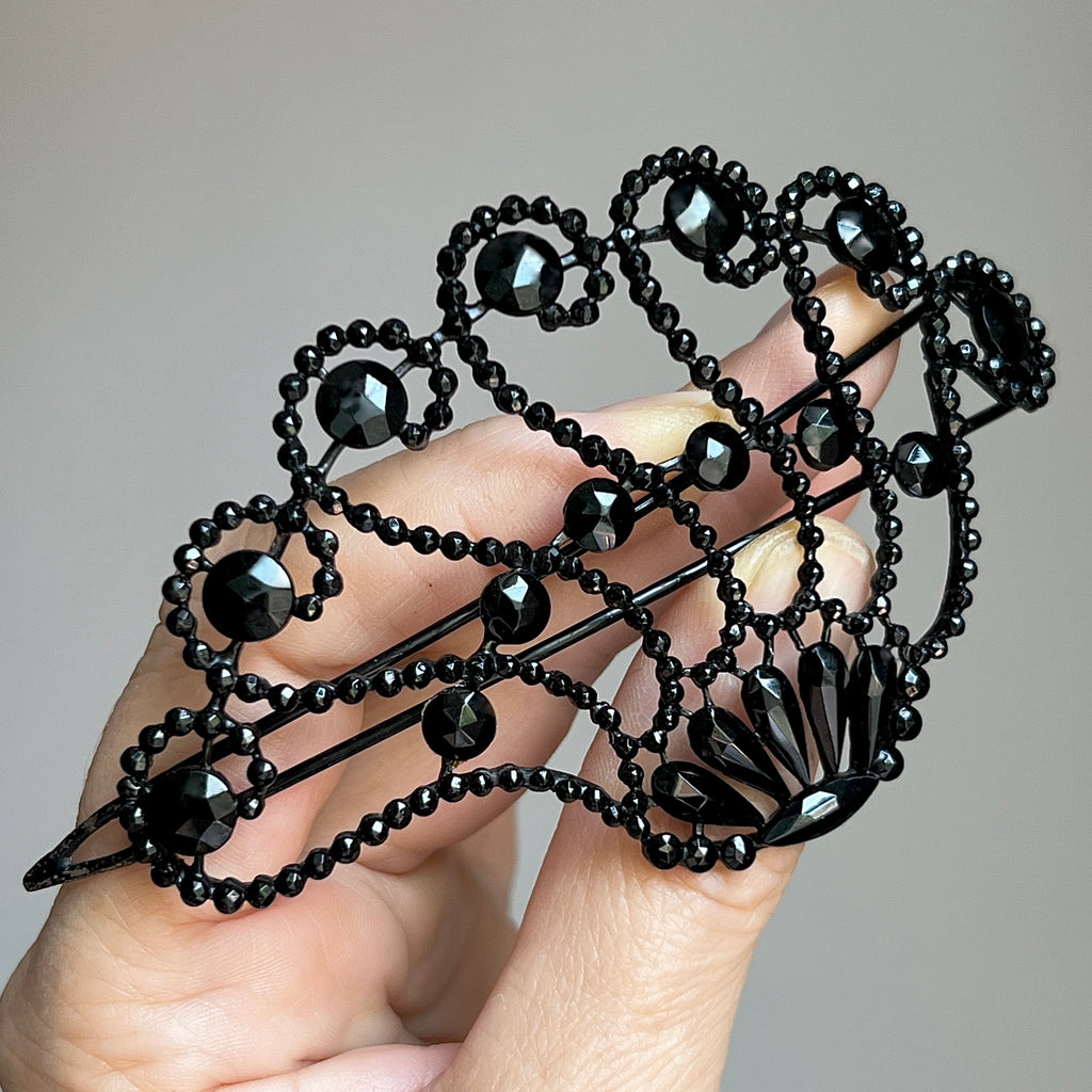 a large antique barrette with small black glass jewels arranged in a lacey scallop design on an openwork wire frame