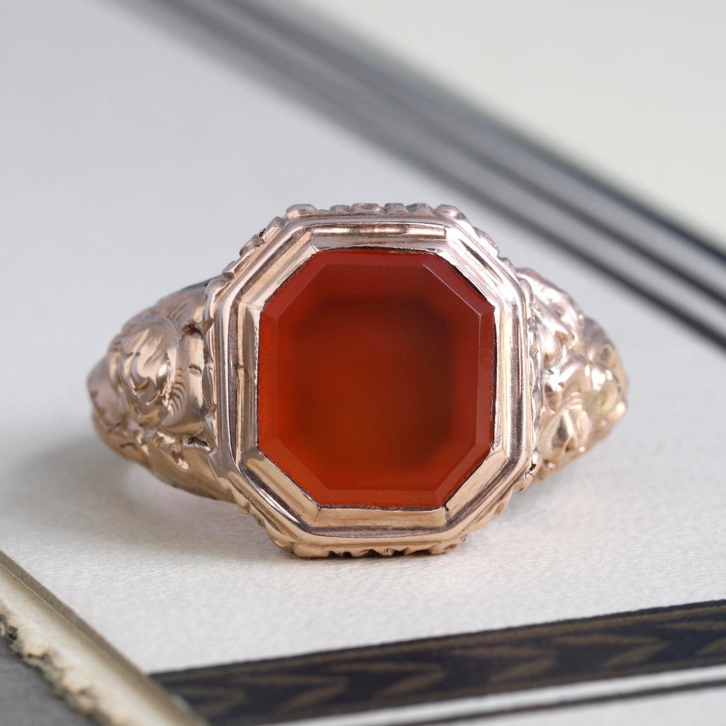 rose gold ring with a fancy floral design embossed on the shoulders and a rust-red carnelian stone set in the front