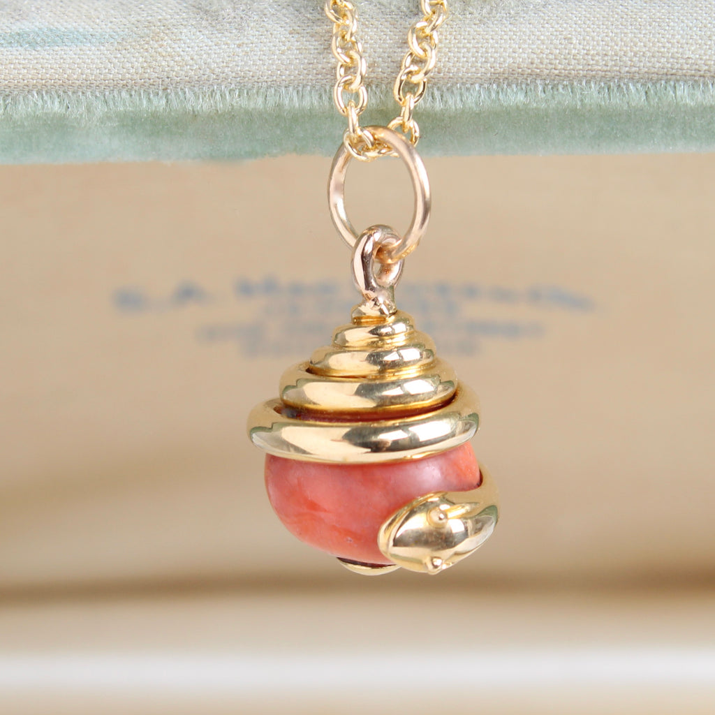 pendant of yellow gold snake coiled around a salmon colored coral ball, on a gold chain