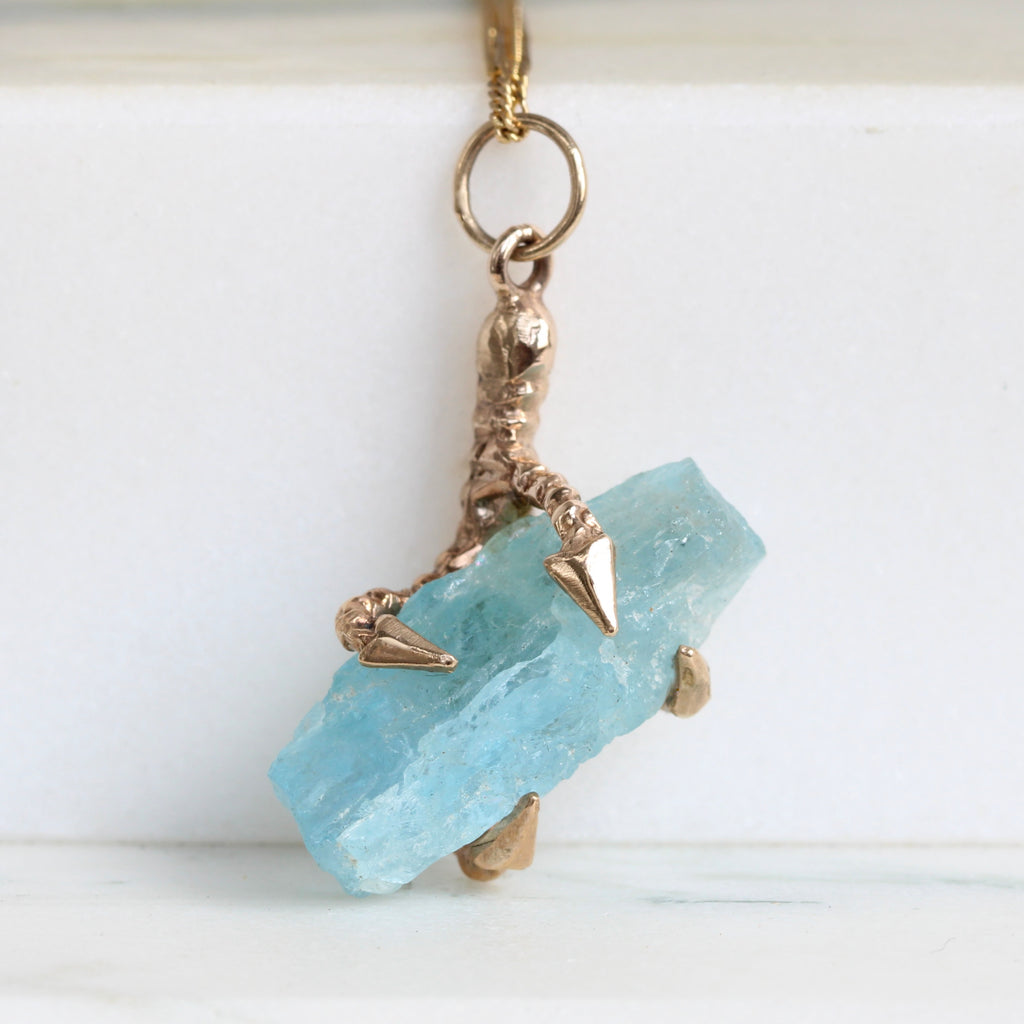 yellow gold claw pendant holding a medium blue natural raw crystal aquamarine 