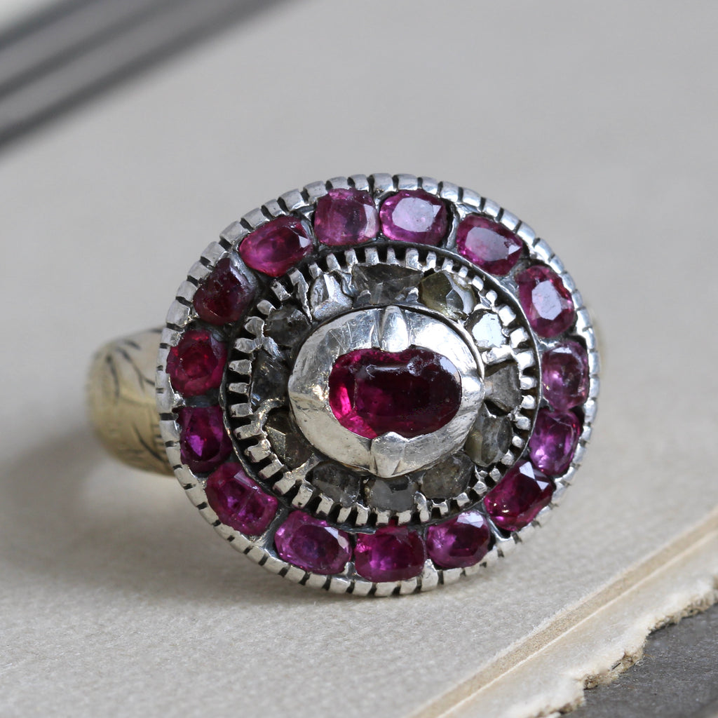 Antique yellow gold ring with a silver bezel holding a ruby center stone, an inner diamond halo, and an outer halo of more rubies.