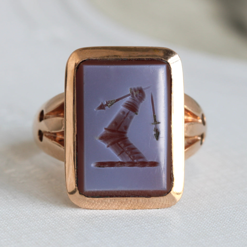 rose gold ring set with a stone carved with a bent arm in armor holding a broken spear