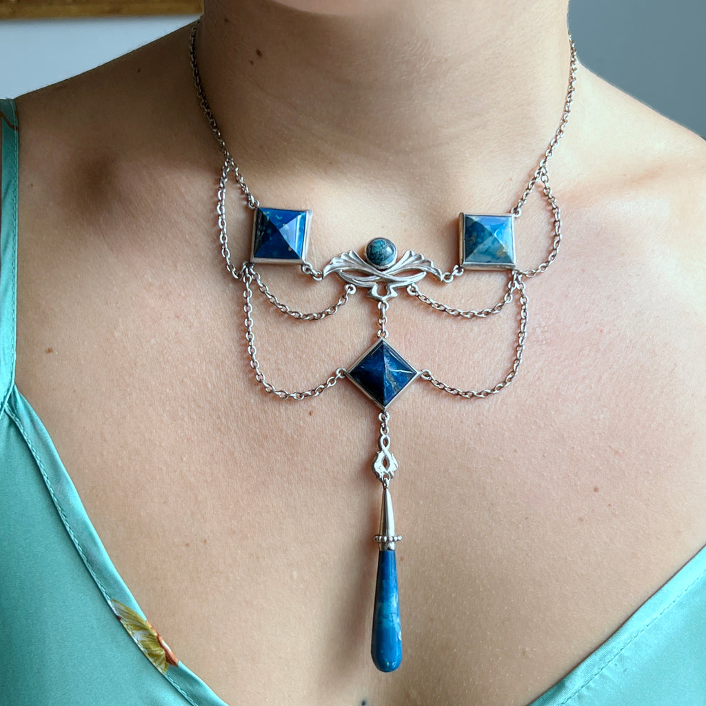 silver ecklace with blue pyramid-shaped pendants and a central blue stone tear drop 