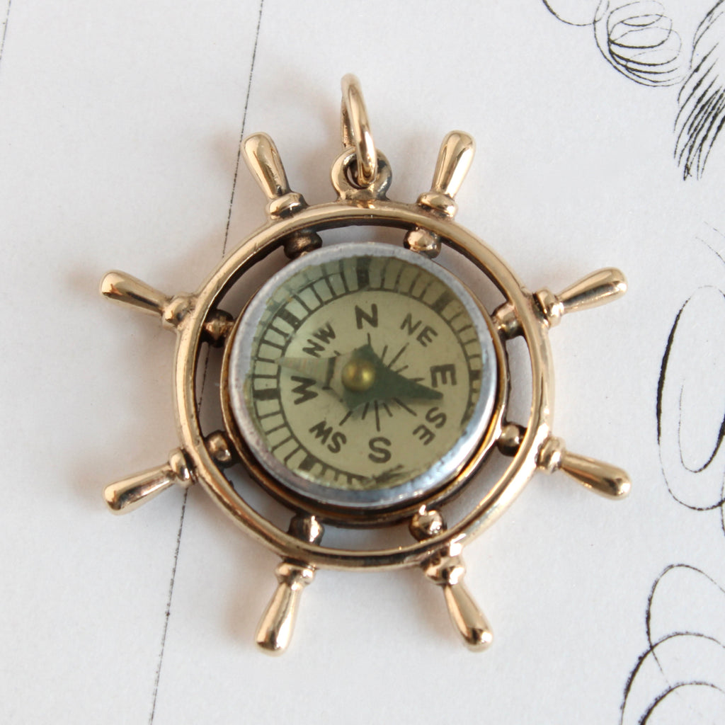 yellow gold pendant designed to look like an ship's wheel with spokes and a miniature compass set in the center