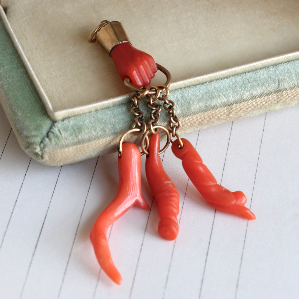 antique carved red coral hand holding a gold loop suspending three coral branch charms