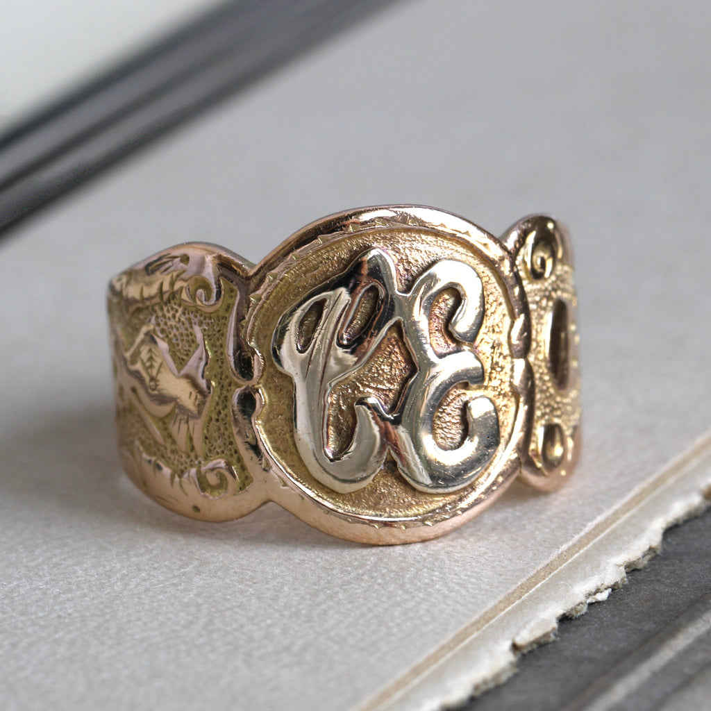 yellow gold wide band signet ring with C.E. intitials on the round face and skull & crossbones and knight helmet embossed on the sides