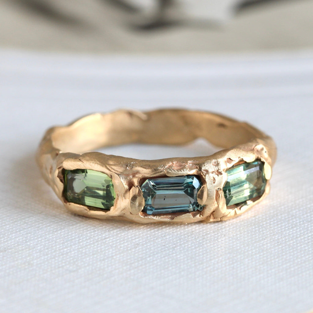 yellow gold band in an organic style with three green and blue sapphire baguettes set across the front