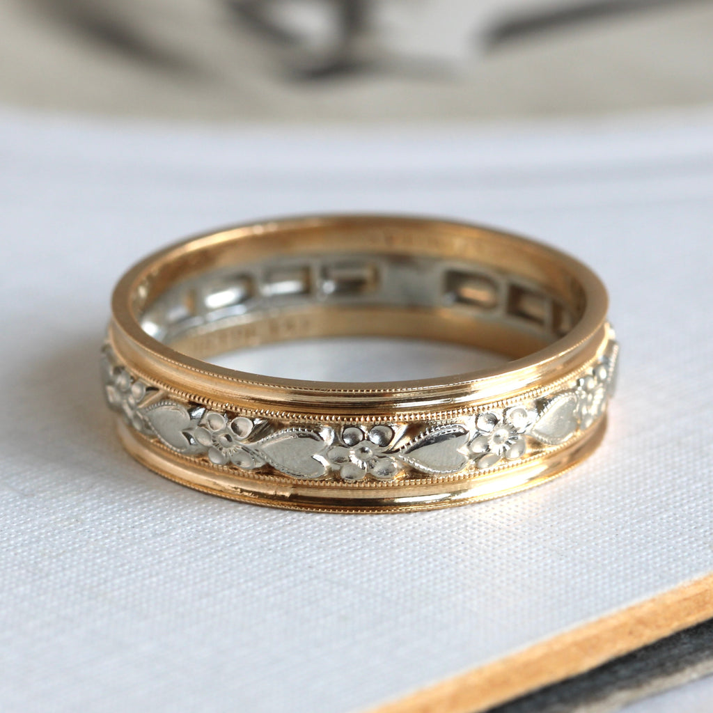  gold wedding band with a middle section of white gold chased in a hearts and flowers design with yellow gold outter sections 