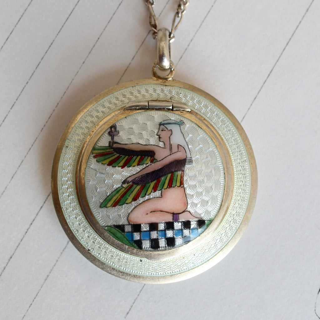 pillbox locket in silver with white enamel backround and a multi color image of a winged egyptian goddess on the cover