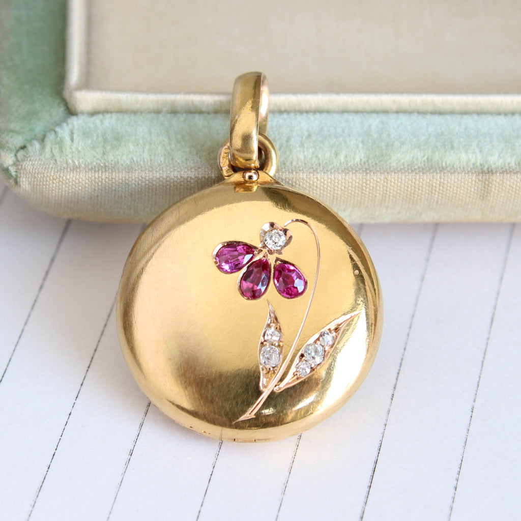 round yellow gold locket with a flower on the cover that's set with pear shaped red rubies and bright old-cut diamonds