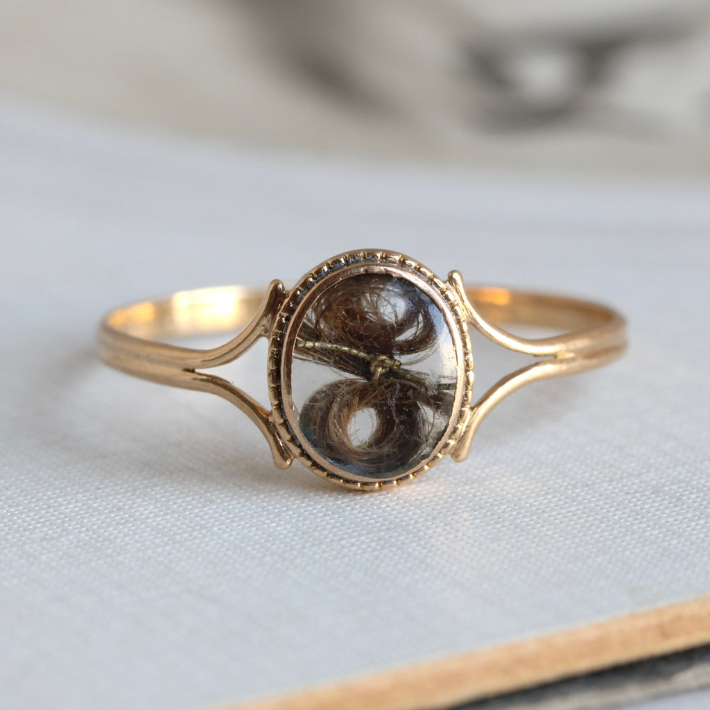 yellow gold ring with a glass locket face hoiding a small lock of brown hair