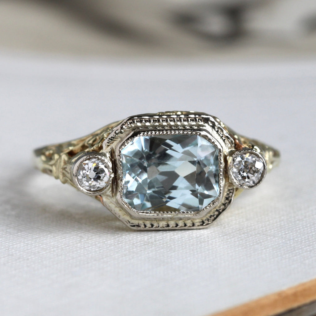 yellow gold filigree ring set with a rectangular pale blue aquamarine with a diamond accent on each side