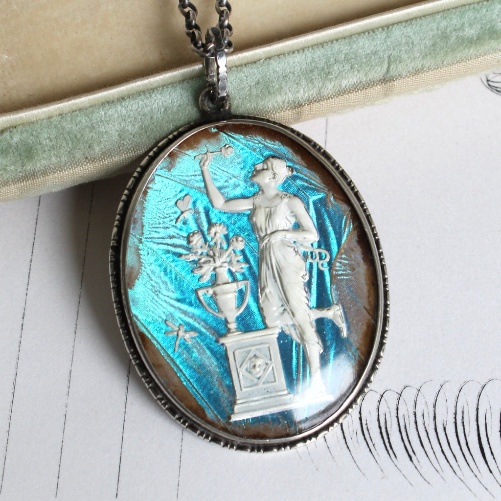 oval pendant with a white cameo of a woman sniffing a rose and an iridescent backround 