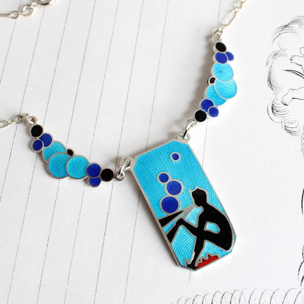 art deco silver necklace with a profile image of pan on his pipes and bubbles in bright shades of blue 