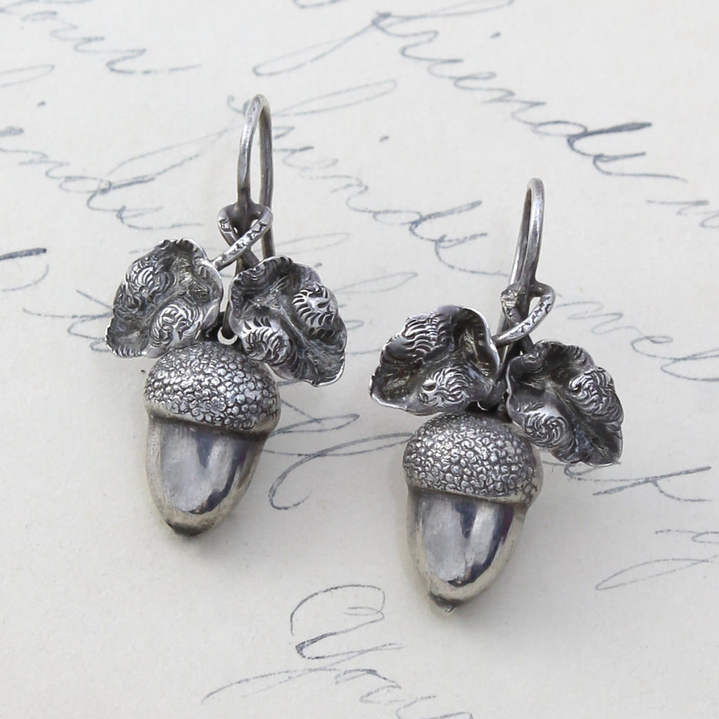 drop earrings of silver designed as acorns dangling below a pair of oak leaves