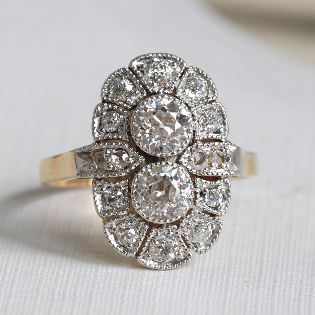 ring with two round diamonds vertically arranged surrounded by a frame of smaller diamonds, all in milgrained platinum with a yellow gold band