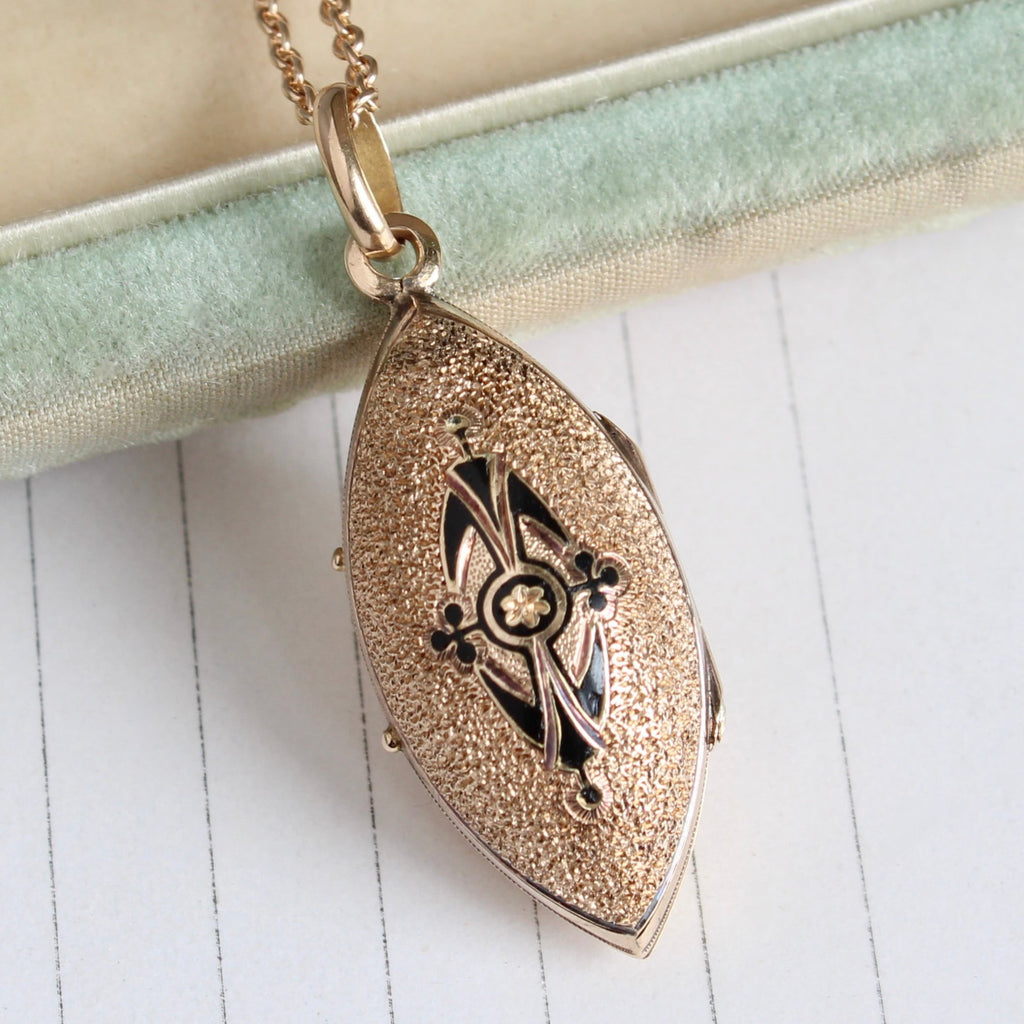 gold locket in a marquise shape with black enamel decoration on the front cover on a chain