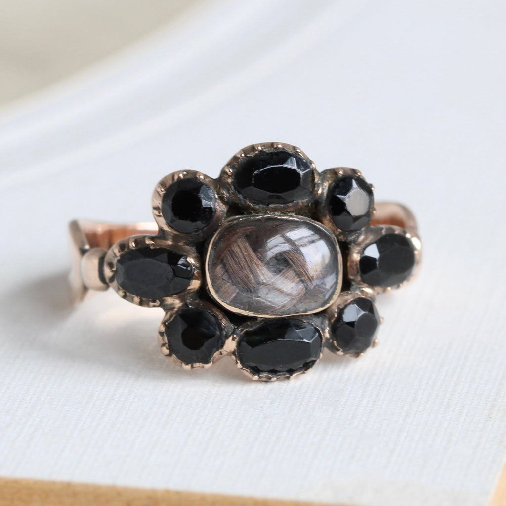 antique rose gold ring with a love knot woven of brown hair under glass, surrounded by faceted black stones, engraved on the back Fred Baury