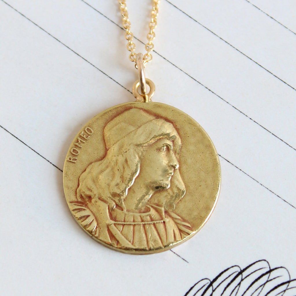 yellow gold medallion charm with a profile portrait of a man in renaissance costume and the name romeo etched around the edge