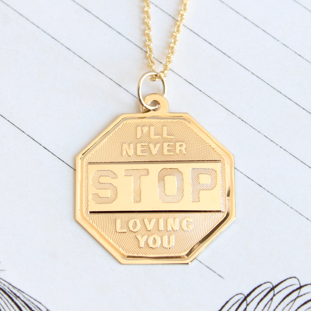 yellow gold stop sign shaped charm with the words I'll never stop loving you" chased across the front.