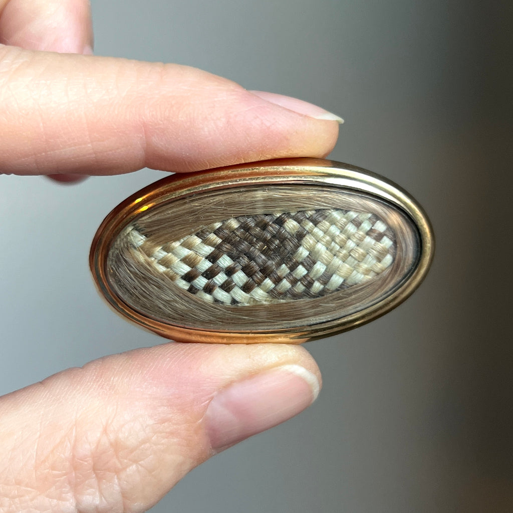 solid yellow gold oval brooch with woven hair under glass.