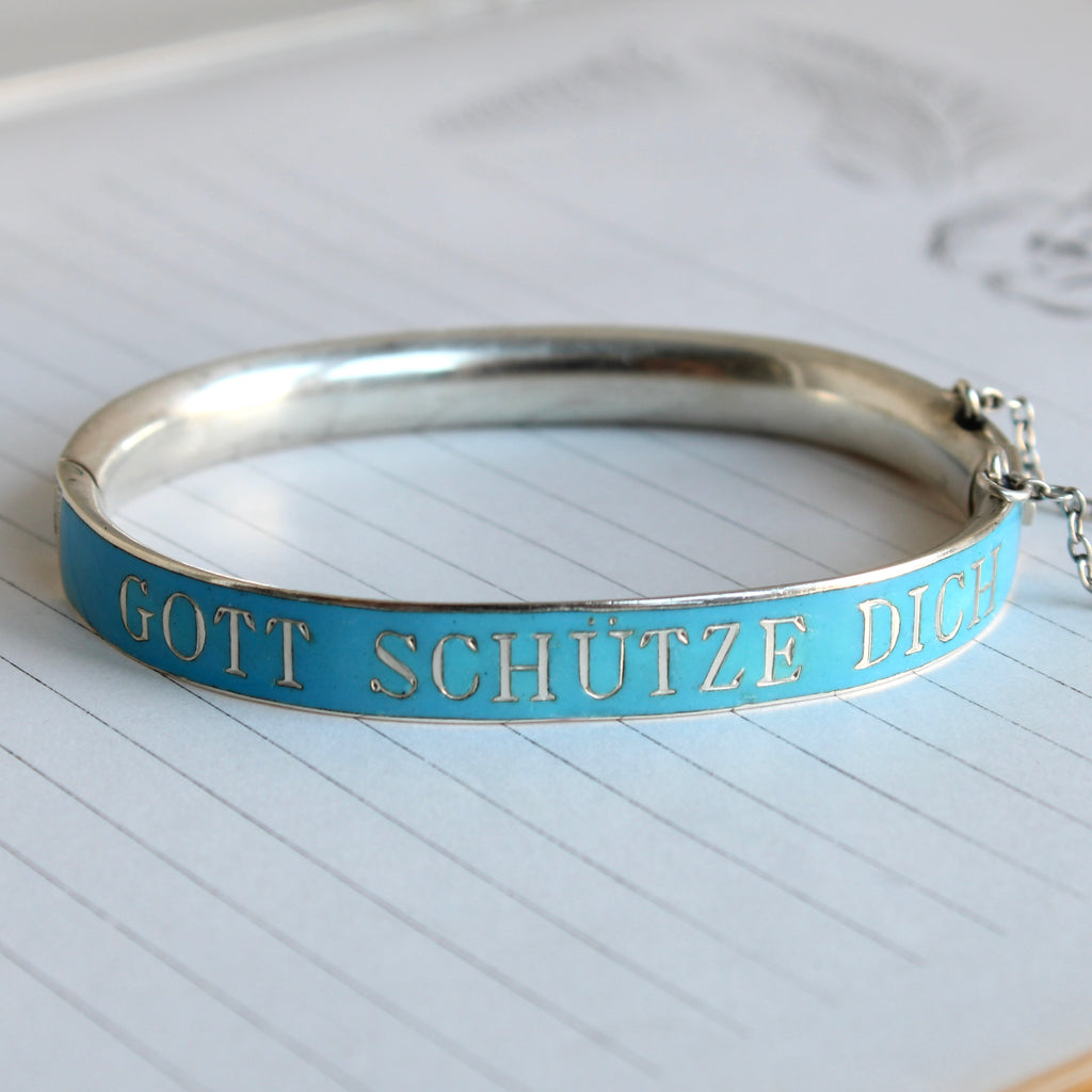 silver bangle bracelet with baby blue enamel all around and the phrase gott schutze dich in silver letters on the front