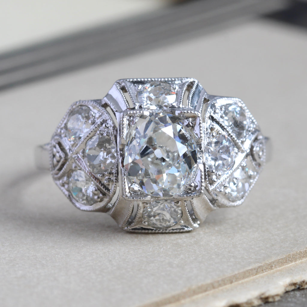 Vintage platinum ring with an old mine cut round diamond center stone in an ornate setting with accent diamonds on all corners.
