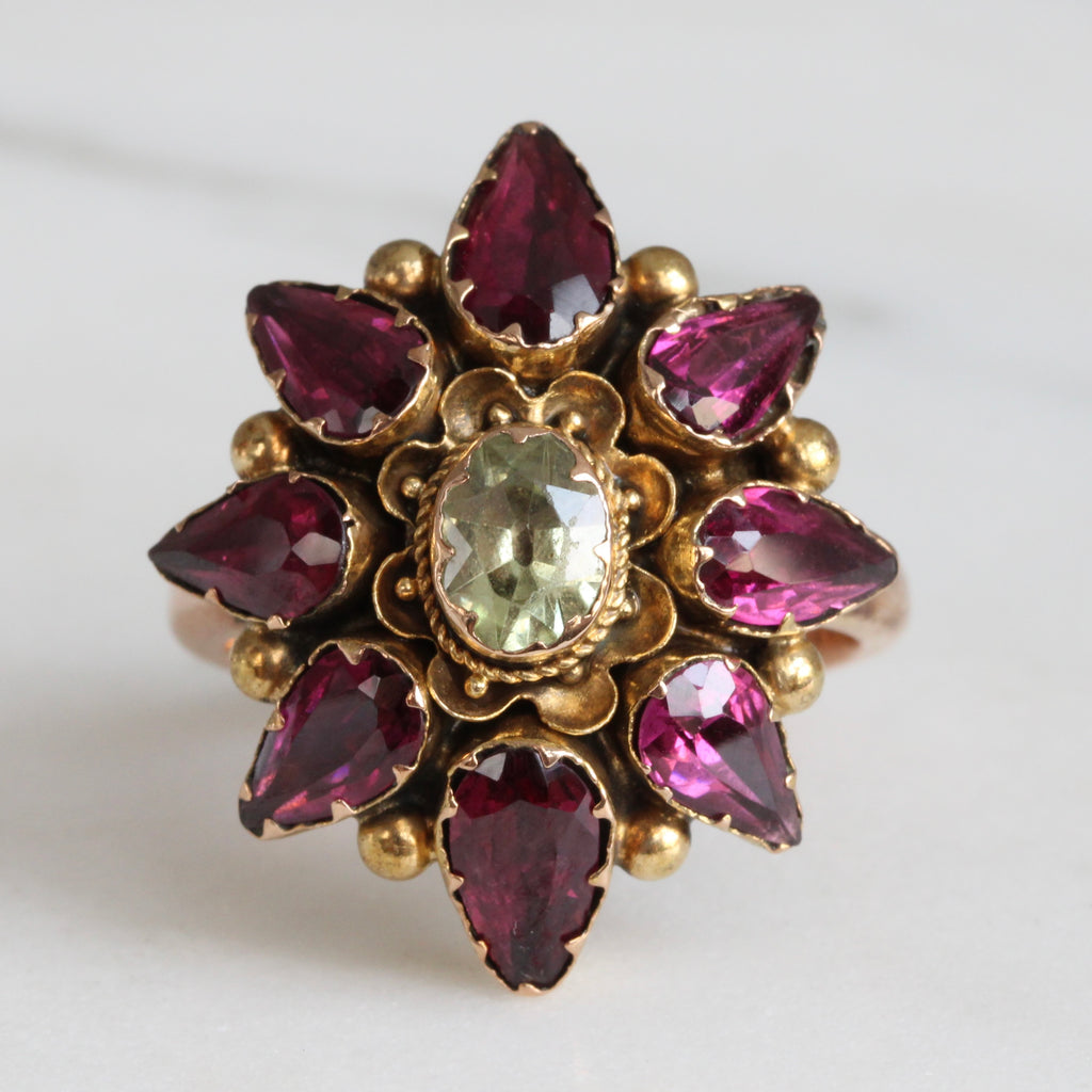 a gold ring with pinkish-red tear drop shaped gems arranged in a cluster around a pale green green gem