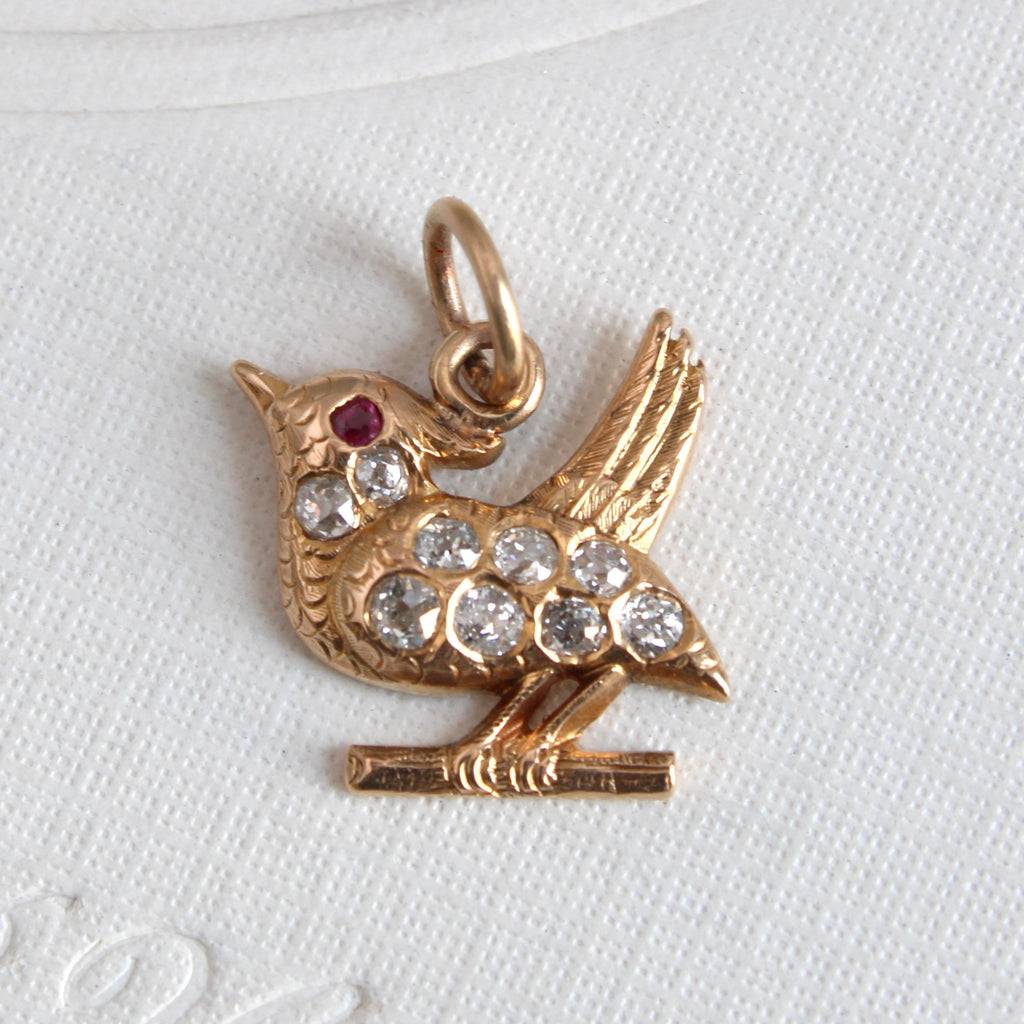 yellow gold bird on a branch charm set all over with sparkling mine cut diamonds and a ruby eye.