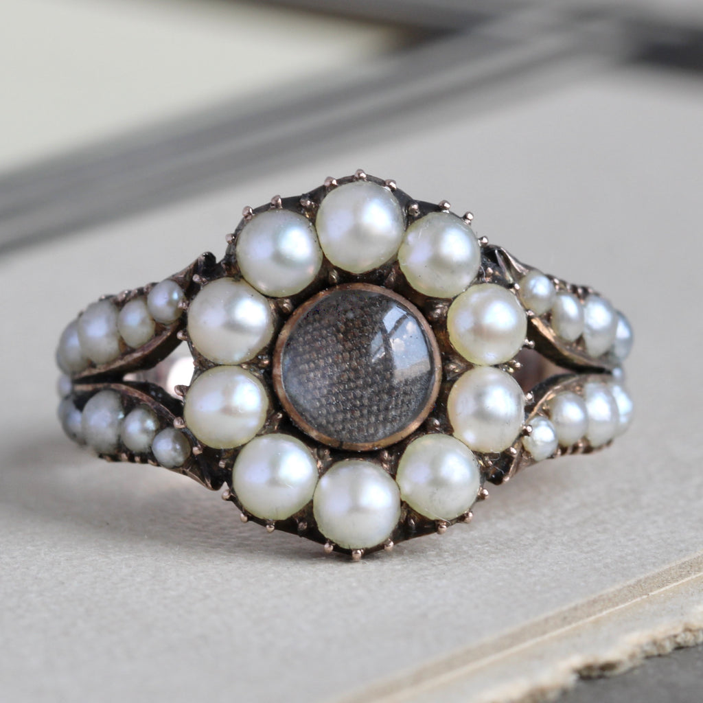 ring from the 1820s designed as a flower with round pearls as the petals and a center of woven hair under glass 