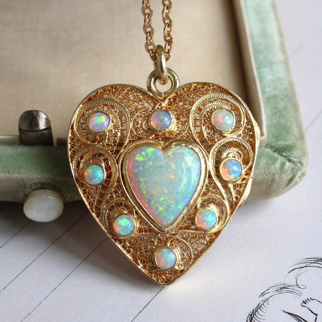 large heart shaped locket made of gold filigree set with a fiery heart shaped opal in the center and small round opal accents