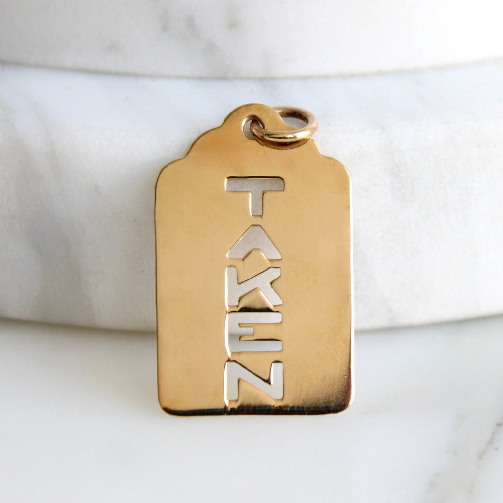 gold pendant shaped like a miliary dog tag with cut out letters reading "taken"