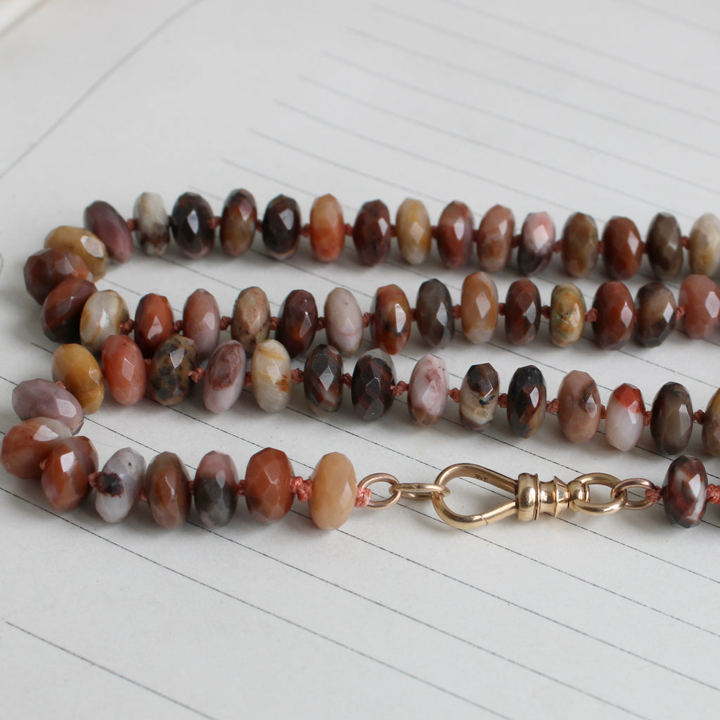 faceted agate beads in a variety of warm earth tone colors knotted on coral colored silk with a gold clip clasp