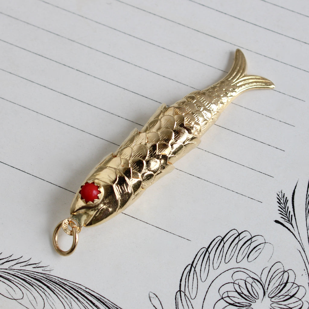 long yellow gold fish charm, hinged so it wiggles, with red coral eyes.