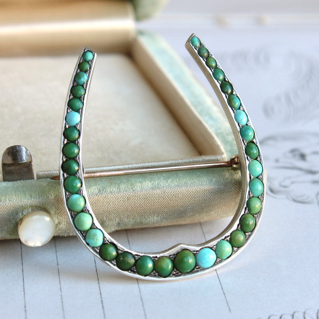 a silver brooch in the shape of a horseshoe set closely with turquoise cabochons in shades of blue and green