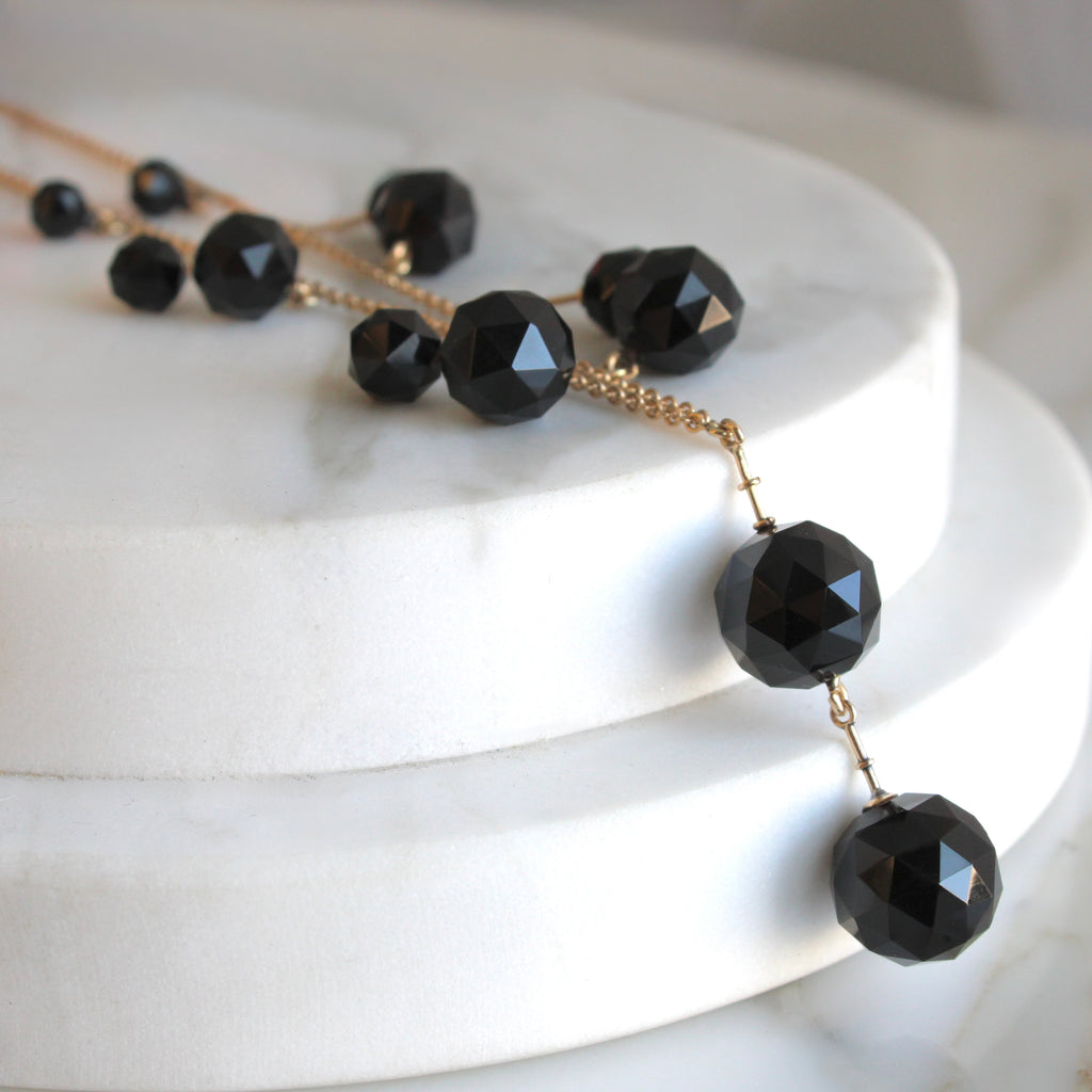 necklace of gold cable chain with a series of faceted black beads attached in a cascade arrangement