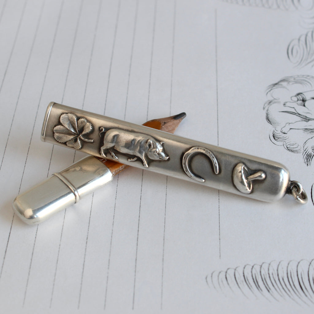 antique pencil in a sterling case with a pig, four leaf clover, mushroom and horseshoe embossed on both sides. Made to wear as a pendant with a bail