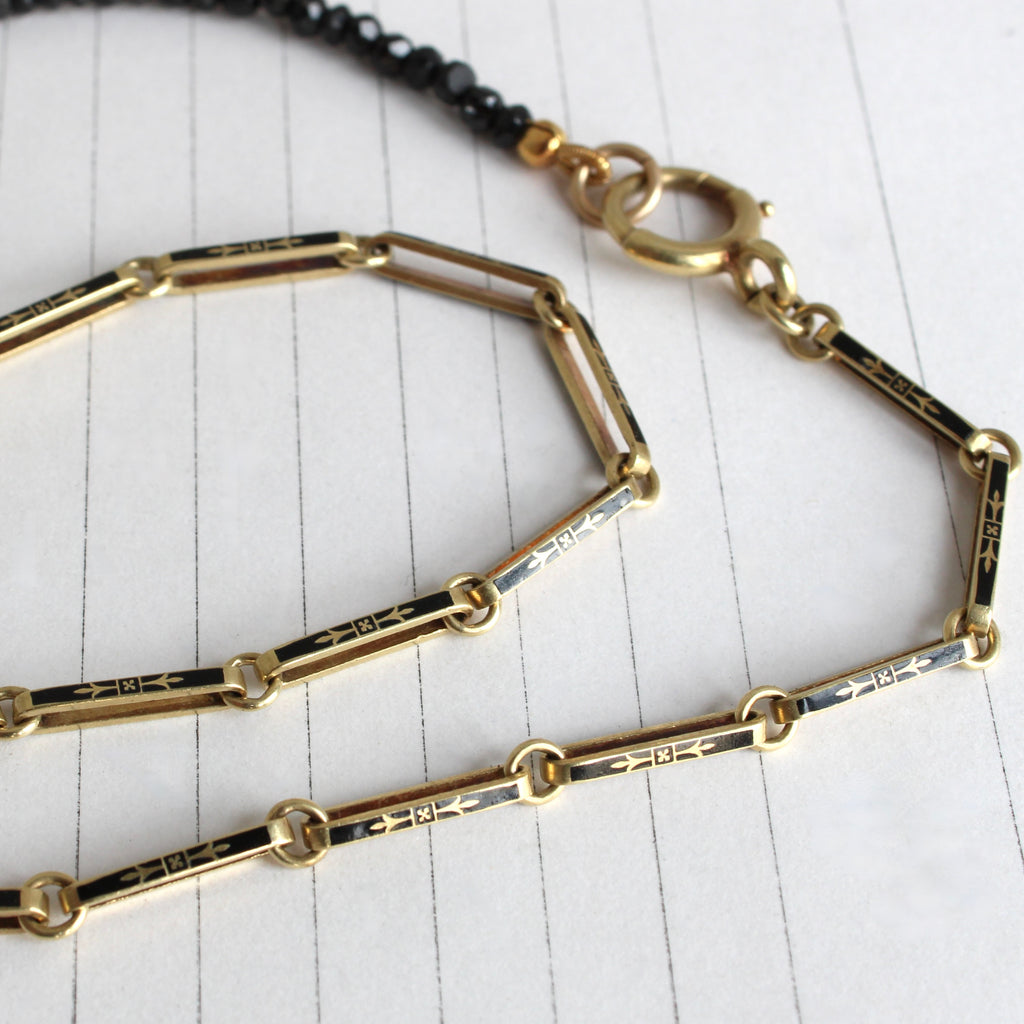 yellow gold chain with bar and round links, a black enamel flower design on the bar links