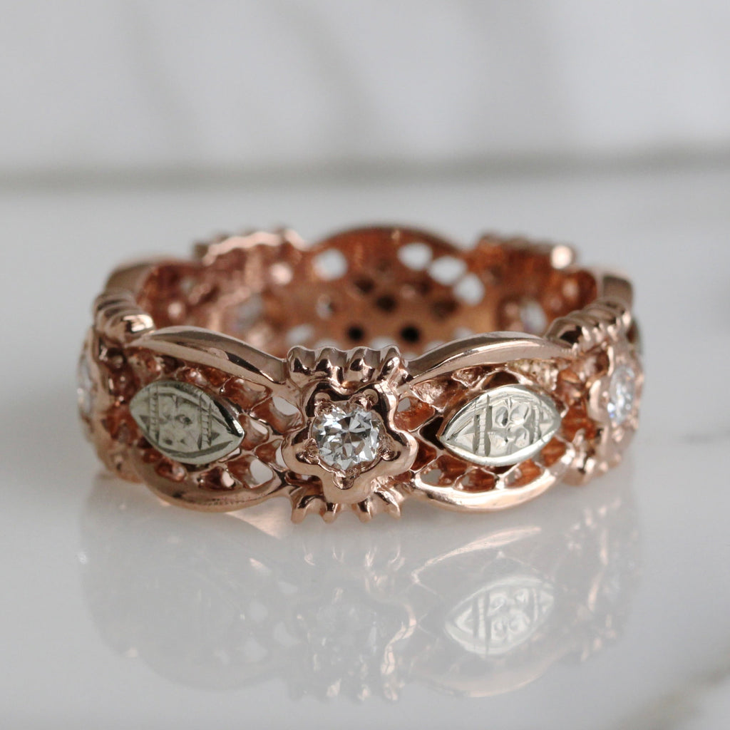 Rose gold ring with a cut out lattice deisgn, diamond accents and flower designs on white gold sections