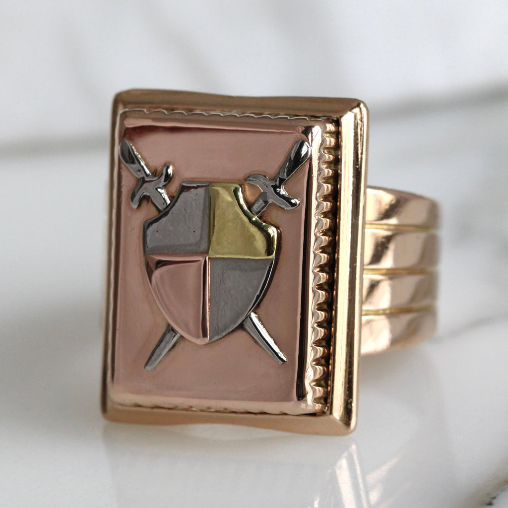 rose gold signet ring with a shield and crossed sword design on the front