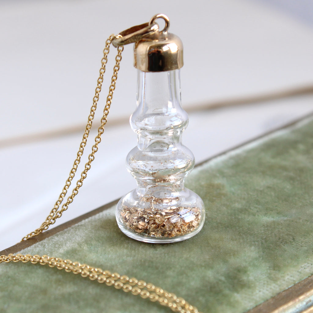 miniature glass bottle pendant with gold flakes inside and a gold cap stopper, on a chain