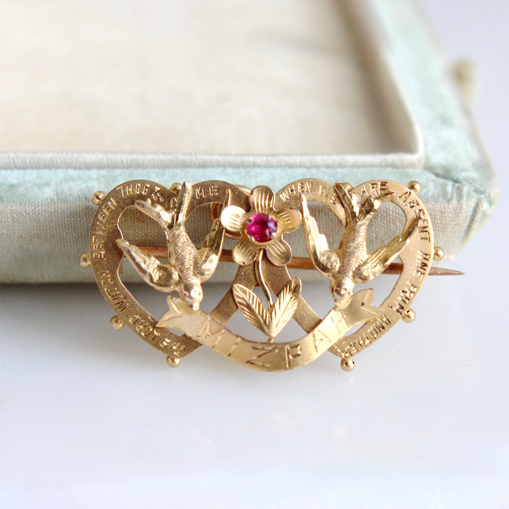 yellow gold brooch with two hearts, two brids and a flower and a hand enrgaved message Mizpah around the edge.