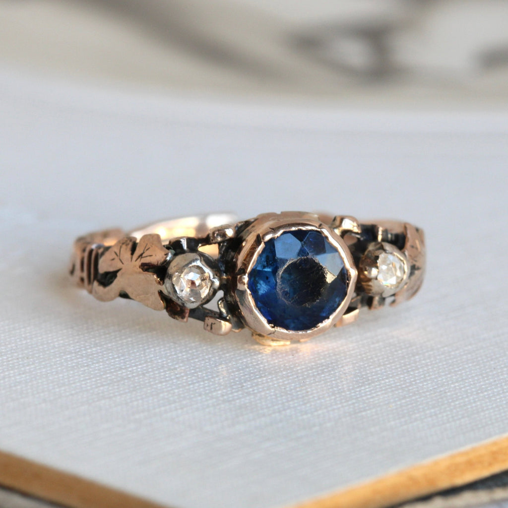 antique ring with a sapphire colored gem in the center, rose cut diamonds at each side and tiny shamrocks on the shoulders