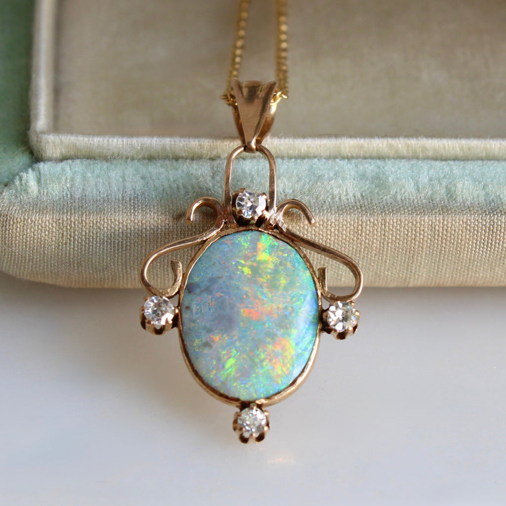 Brightly multi-colored oval stone with yellow and orange flashes set in gold as a pendant with four diamond accents, on a gold chain