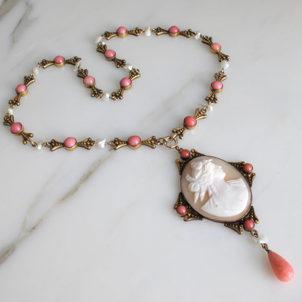 a yellow metal necklace with a carved portrait of a woman in light brown and white shell and coral colored stone accents