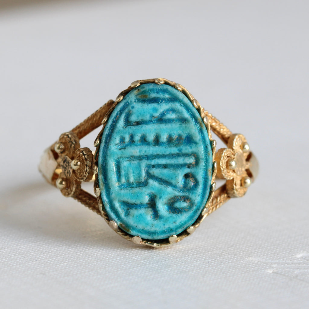 yellow gold ring set with an oval blue-green ceramic face  carved with egyptian symbols or hieroglyphs